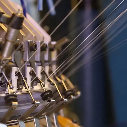 Raising Machine, showing multiple white threads running through metal yarn guides during the manufacturing process