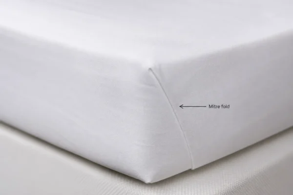 Close-up of a perfectly formed hospital corner tuck on a crisp white flat sheet on a hotel bed mattress