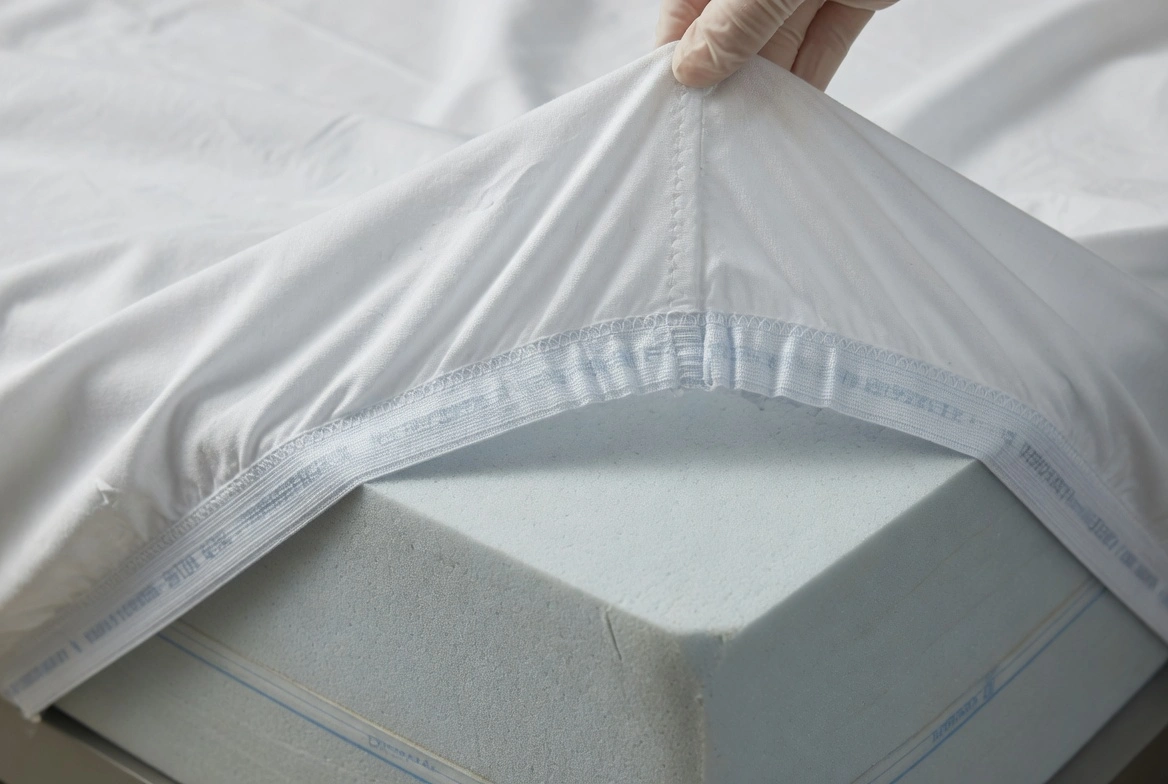 Close-up of reinforced deep elastic corner pocket on a white hospital bed fitted sheet, 8-inch pocket depth