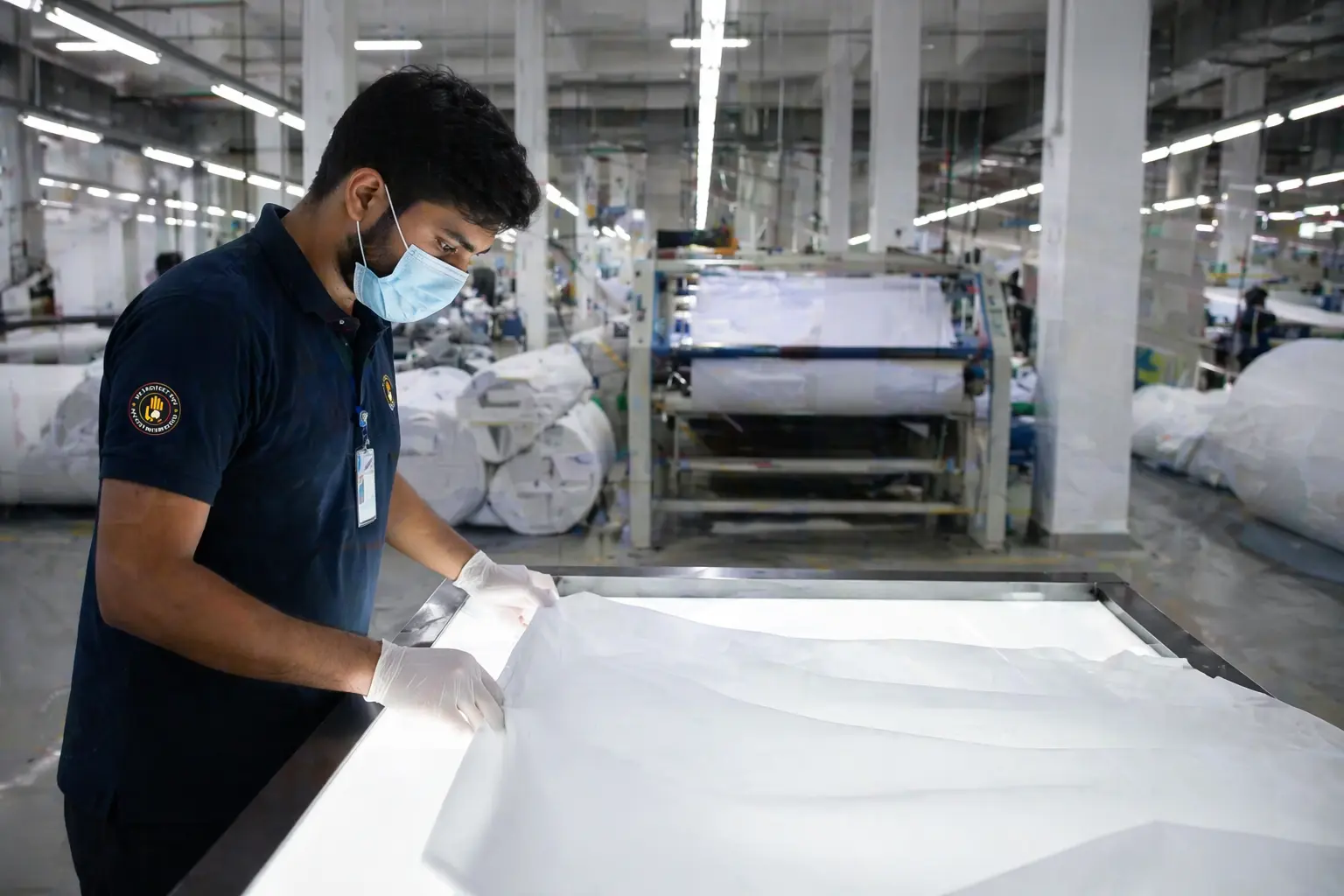 Quality control inspector examining white hospital bed sheet fabric in an ISO 9001 certified textile factory in Faisalabad Pakistan