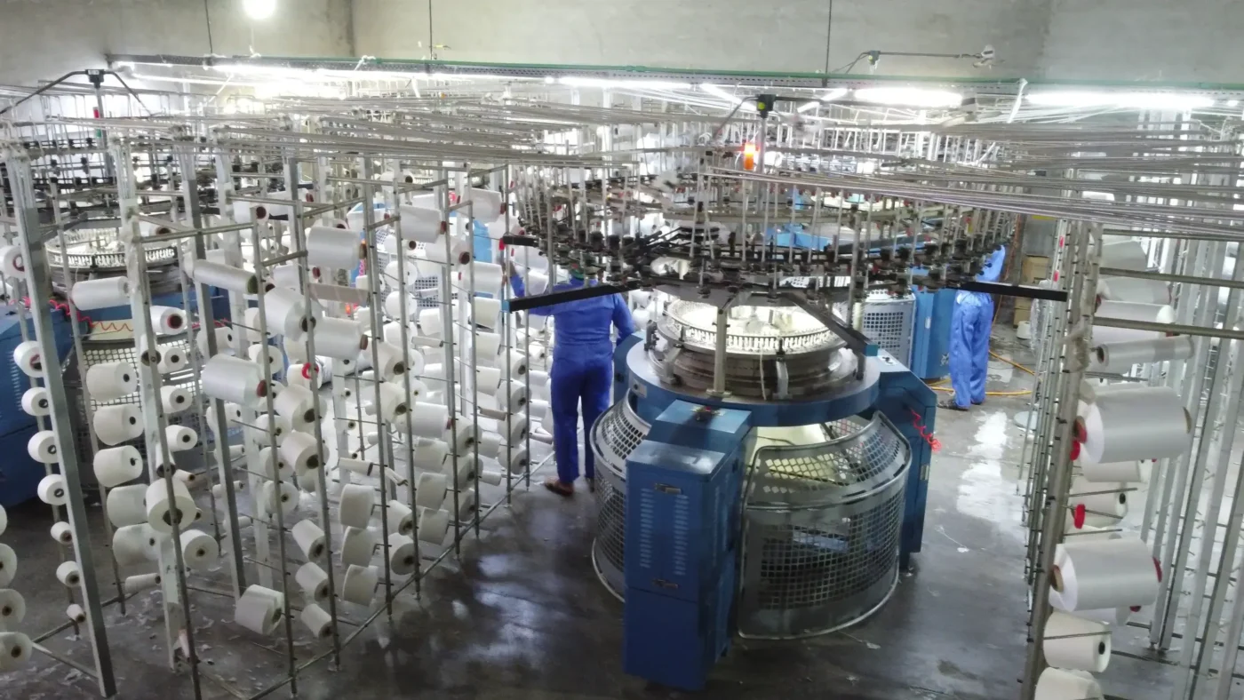 Interior of a professional textile manufacturing facility with industrial knitting machines producing socks, clean factory floor in Faisalabad Pakistan