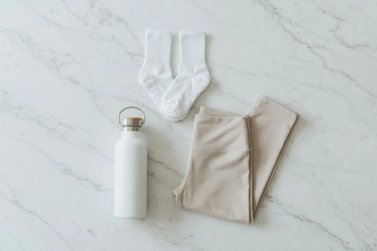 Flat lay of lagree class essentials — full-toe grip socks, a water bottle, and minimal workout clothing arranged on a light wooden surface ready for a lagree class