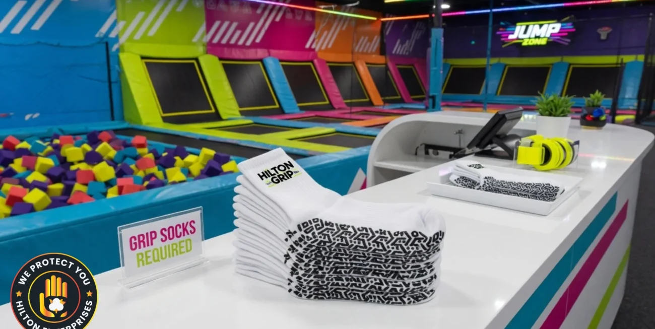 Custom branded white grip socks with bold PVC grip pattern displayed at a modern trampoline park entry desk with colourful park branding visible in the background